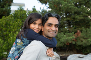 Little girl smiling on Dad's back with greenery backdrop