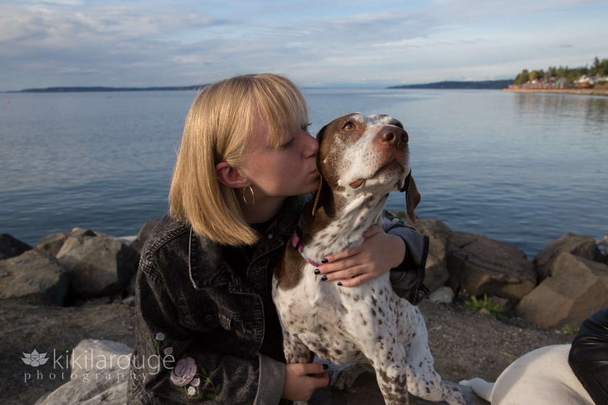 Blonde girl kissing her German Pointer dog on rock at beach