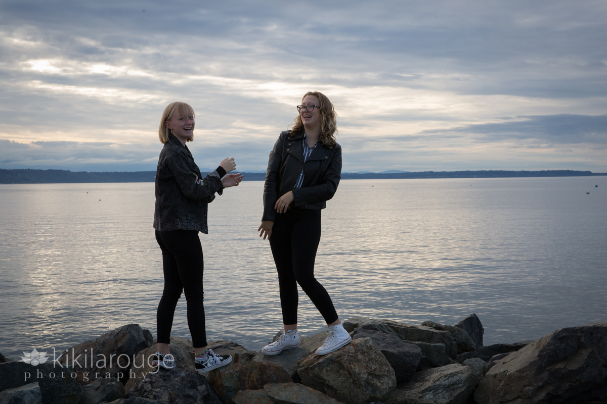 Two teen girls laughing on rocks with sunset background