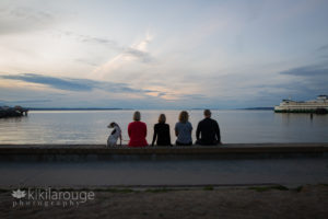 Family sitting on breakwater wall looking out at water and sunset