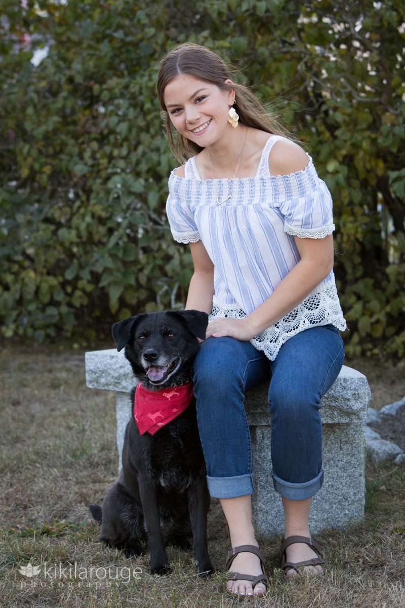 Teen girl sitting on marble stool with black dog by her side