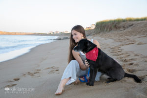 Teen girl sitting on beach with black dog both looking in distance