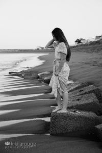 Teen girl in dress on rocks a beach looking down