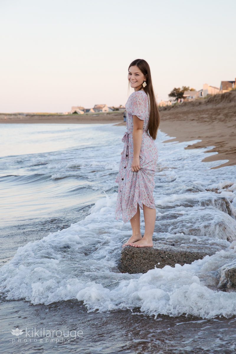 Teen girl long hair in dress smiling on rocks at beach