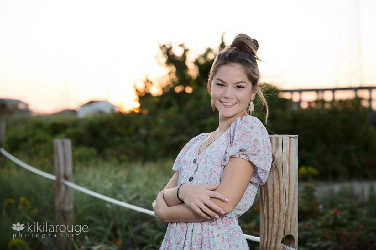 Senior girl with hair in bun smiling and leaning on post at sunset