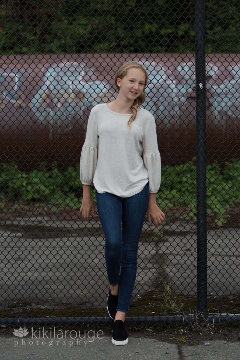 Teen girl in jeans leaning on black chain link fence
