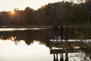 Silhouette of family with dog on dock at pond sunsest