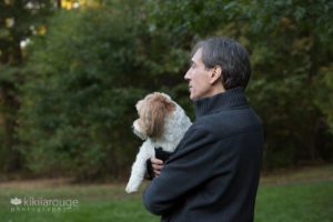 Man in grey sweater holding havanese dog looking away profile