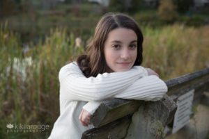 Teen girl in white sweater leaning on bench by pond