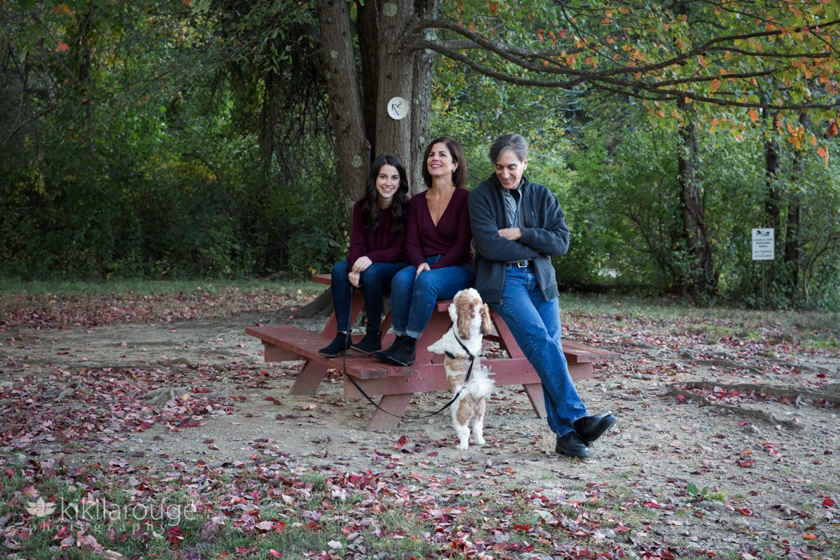 Family sitting on red picnic bench under autumn tree with dog