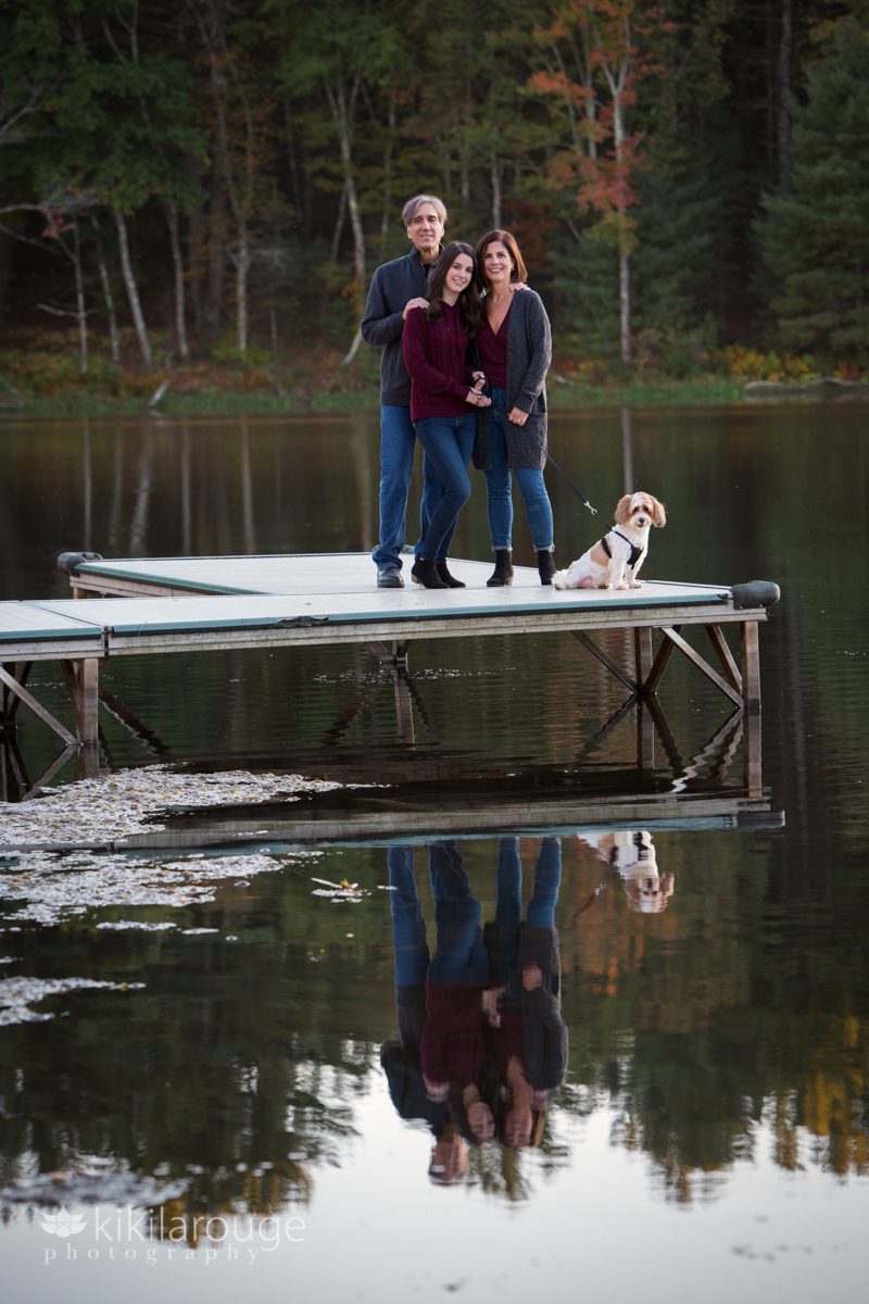 Family of three with dog and reflection in pond at autumn sunset