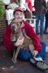 Close up portrait of light brown pit bull rescue dog in arms of person with red sweatshirt sitting on brick sidewalk