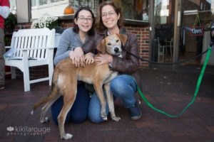 Tan and white hound mix rescue dog with two women on sidewalk