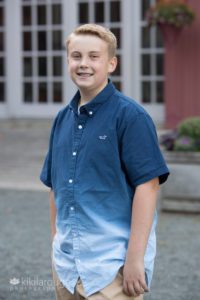 Young boy with braces and blue button up shirt by farm
