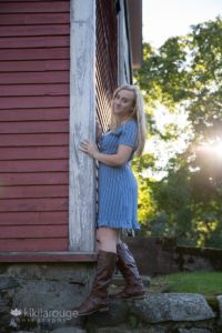 Girl in blue dress and brown boots climbing the side of red barn