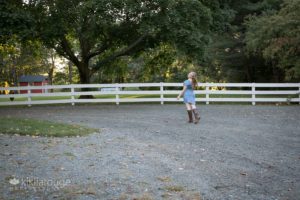 Girl walking away smiling over her shoulder with white fence in background at farm