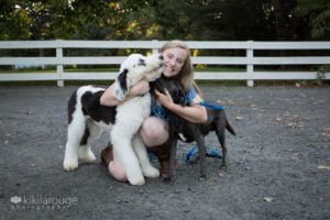 Girl getting kisses by a white sheep and brown rescue dog