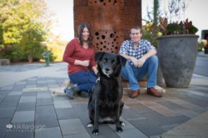 Cute photo of black dog with brown eyes and his parents in background