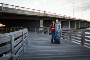 Couple with black dog on wooden bridge at sunset