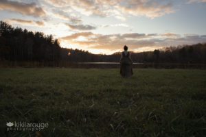Young girl walking through field towards pond at sunset