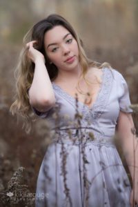 Girl in field with with pastel purple dress with hand in her hair