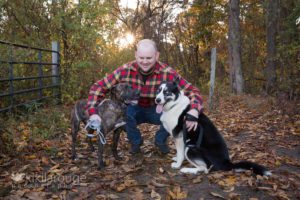 Man in plaid shirt with two rescue dogs in woods at sunset