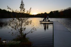 Couple at end of small dock silhouette at sunset with two rescue dogs