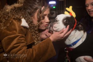 Woman with curly hair kissing a dog with a yellow unicorn horn