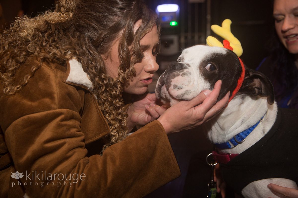 Woman with curly hair kissing a dog with a yellow unicorn horn