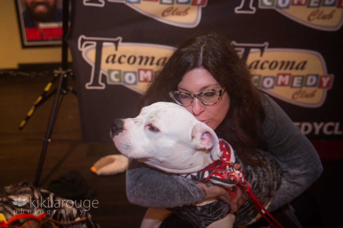 Woman in horn rimmed glasses kissing small white pit bull mix dog