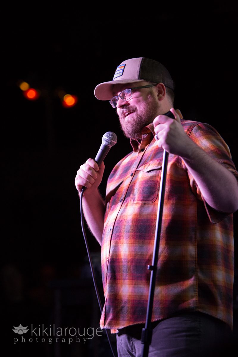 Comedian telling joke on stage in flannel shirt and trucker hat