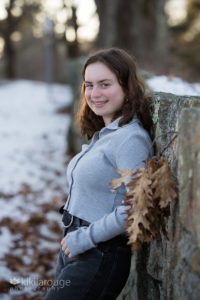 Portrait of a girl in grey top leaning on stone wall winter