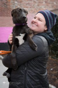 Woman holding a black and white rescue dog by brick wall