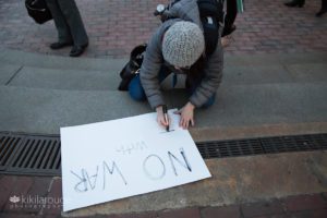 Women at anti war protest writing a NO WAR sign on ground