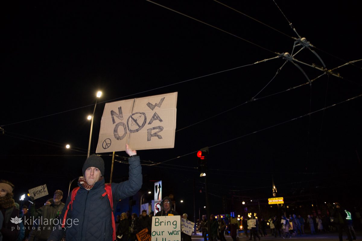 Man holding a NO WAR sign up in the night sky