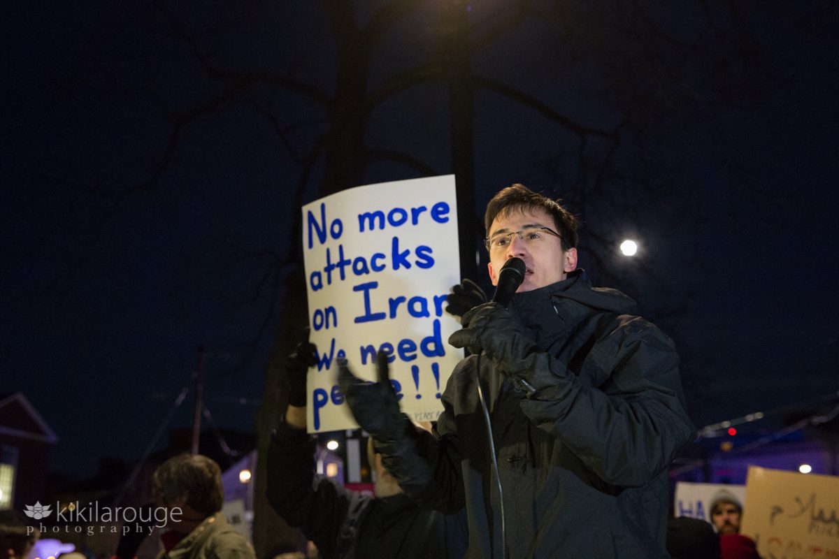 Man in black winter coat leading anti war chants at night Harvard