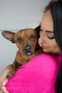 A tan rescue dog in arms of foster mom in pink with tongue out
