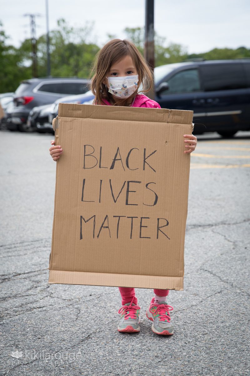 Young girl holding cardboard Black Lives Matter poster in parking lot