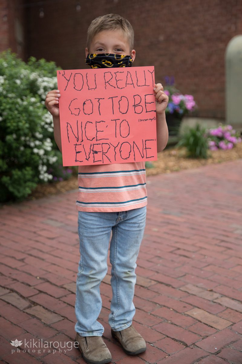 Young boy holding up a sign to be nice to everyone at protest