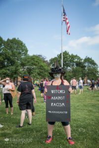 Woman in witches hat with "Witches Against Facism" sign Salem MA