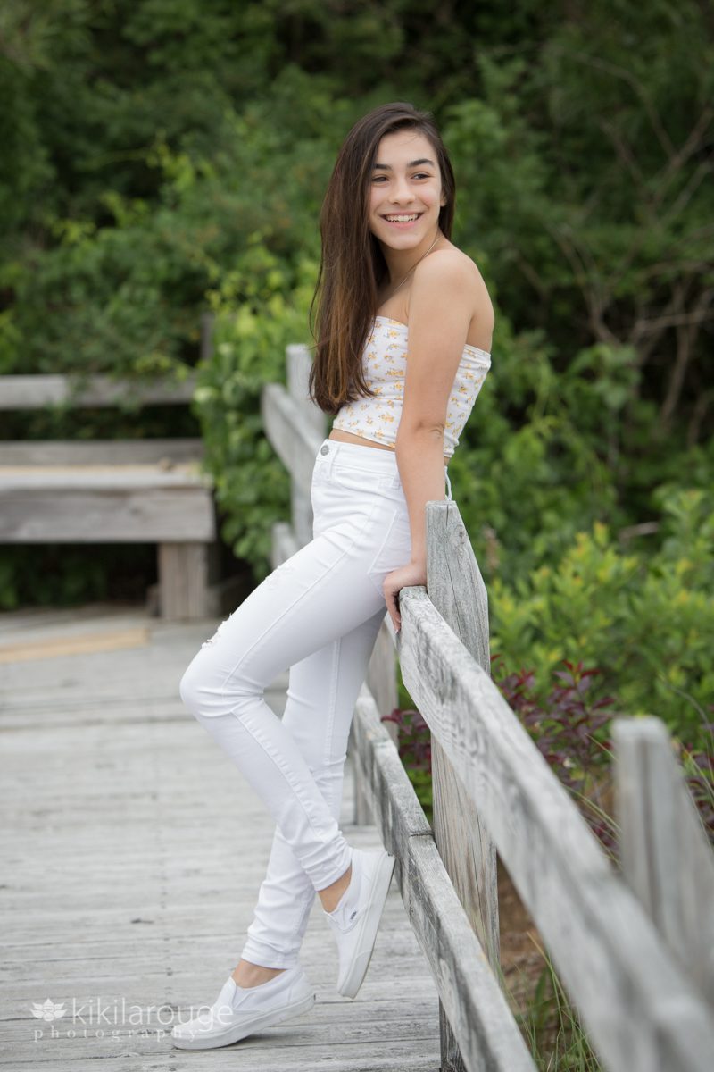 Teen girl brunette in white jeans with tube top leaning on beach boardwalk