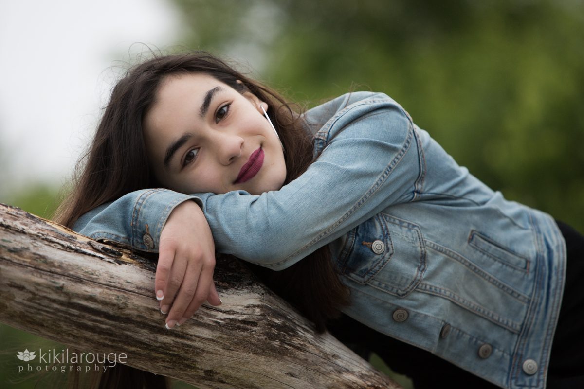 Teen girl leaning on driftwood in denim jacket
