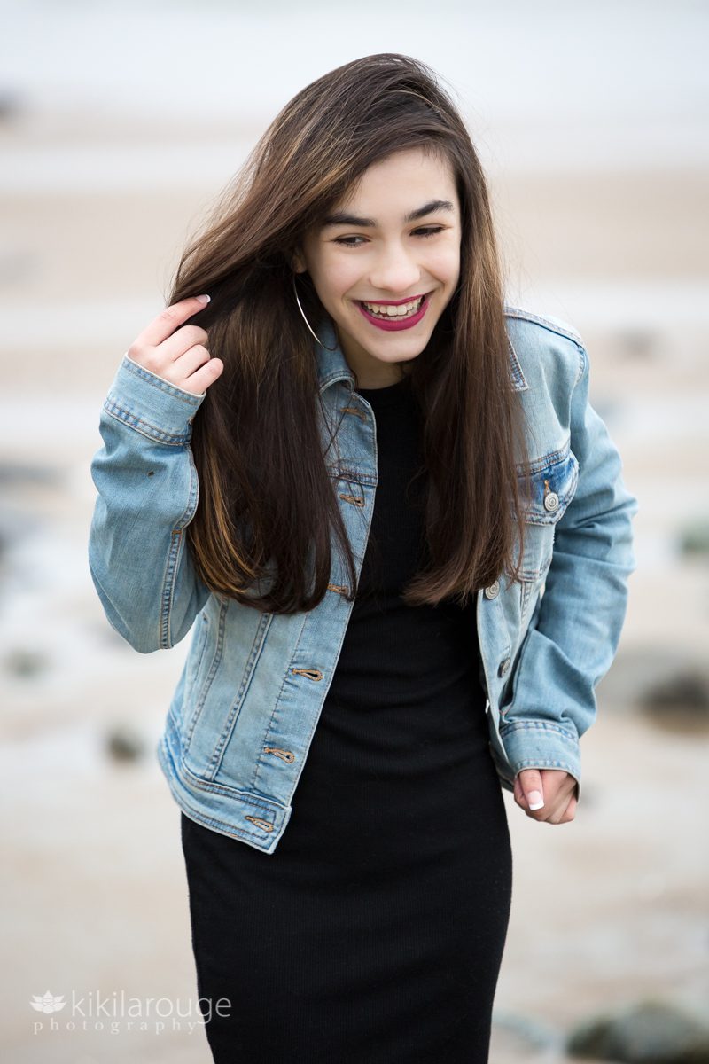 Girl looking down smiling holding back hair in denim jacket and black dress