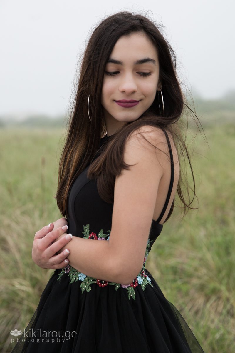 Teen girl in black dress smiling looking down in beach dunes