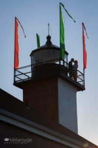 Couple on top of brick lighthouse kissing with flags blowing