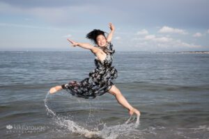 Teen girl jumping in air in dress at water's edge