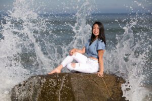 Girl sitting on rock with huge wave crashing
