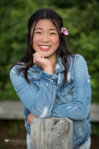 Teen girl senior portrait with beach rose in hair leaning on driftwood