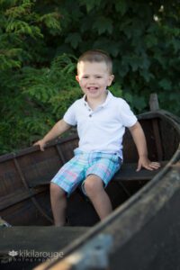 Toddler boy in plaid shorts sitting in brown boat