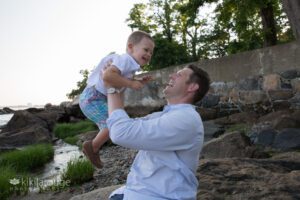 Dad smiling holding up toddler son in the air at beach